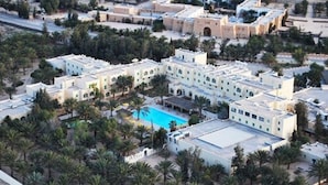 An aerial view of a hotel complex with multiple buildings, a swimming pool, and surrounding palm trees. - Hotel Sahara Douz (Douz Nord)