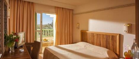 A hotel room with a large bed, a wooden desk with a chair, a television, and a balcony with curtains.