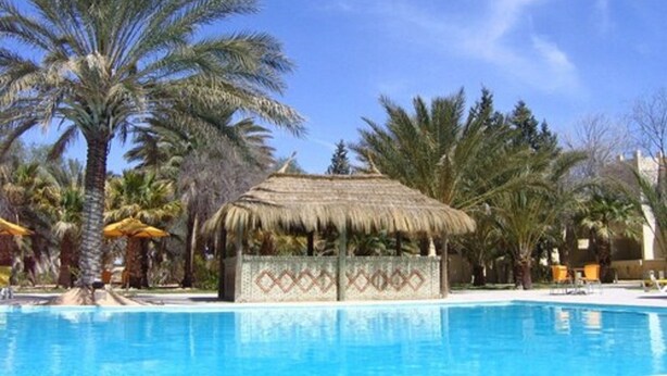 A swimming pool surrounded by palm trees and a thatched-roof structure. - Hotel Sahara Douz (Douz Nord)