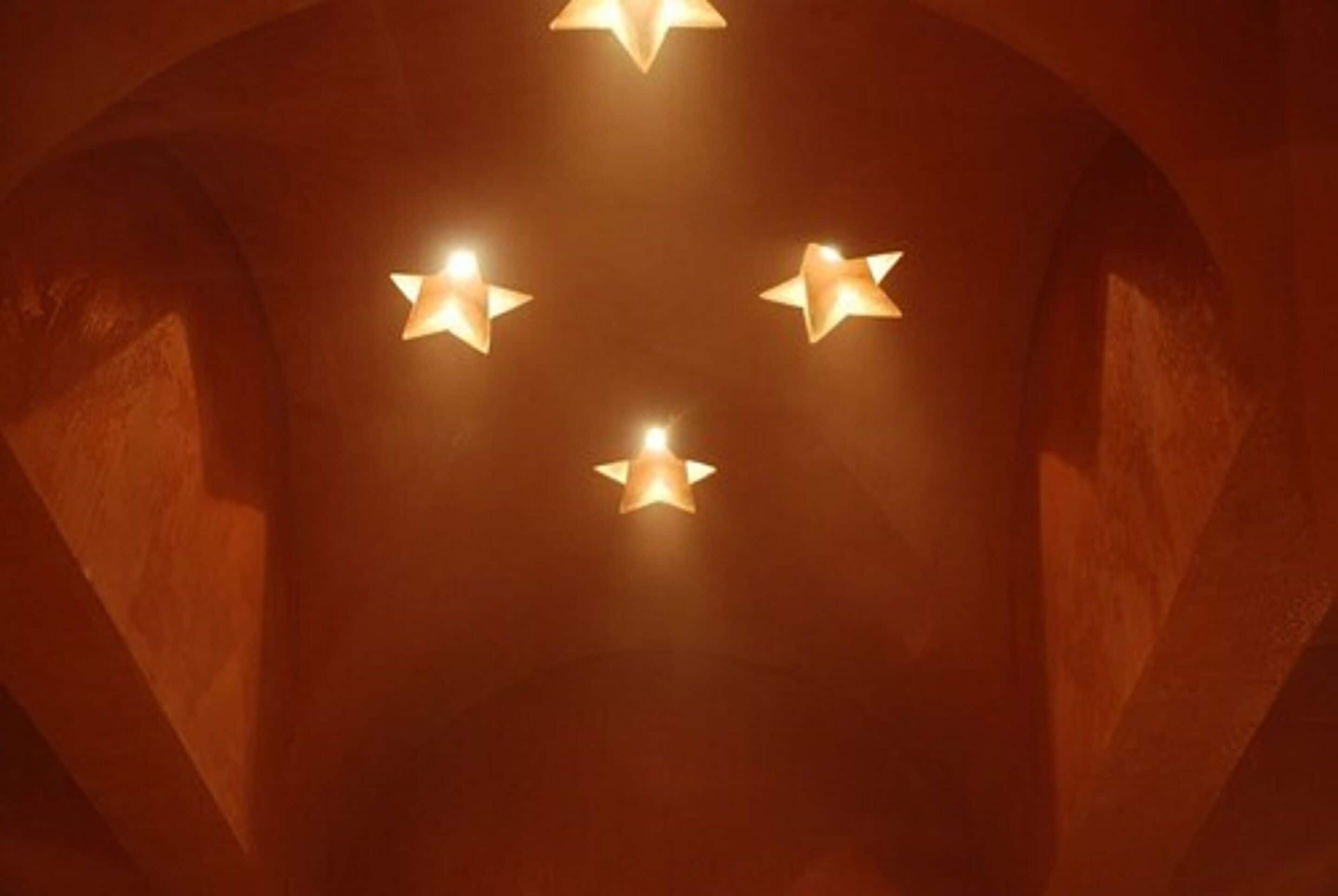 A ceiling with four star-shaped lights in a dimly lit room with arched ceilings.