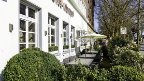 A hotel with a white facade, large windows, and outdoor seating with umbrellas. - Art Hotel Monopol (Gelsenkirchen)
