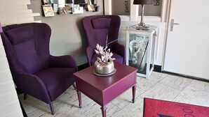 A room with two purple armchairs, a small table with a vase, a mirror, and a door with a sign. - Art Hotel Monopol (Gelsenkirchen)
