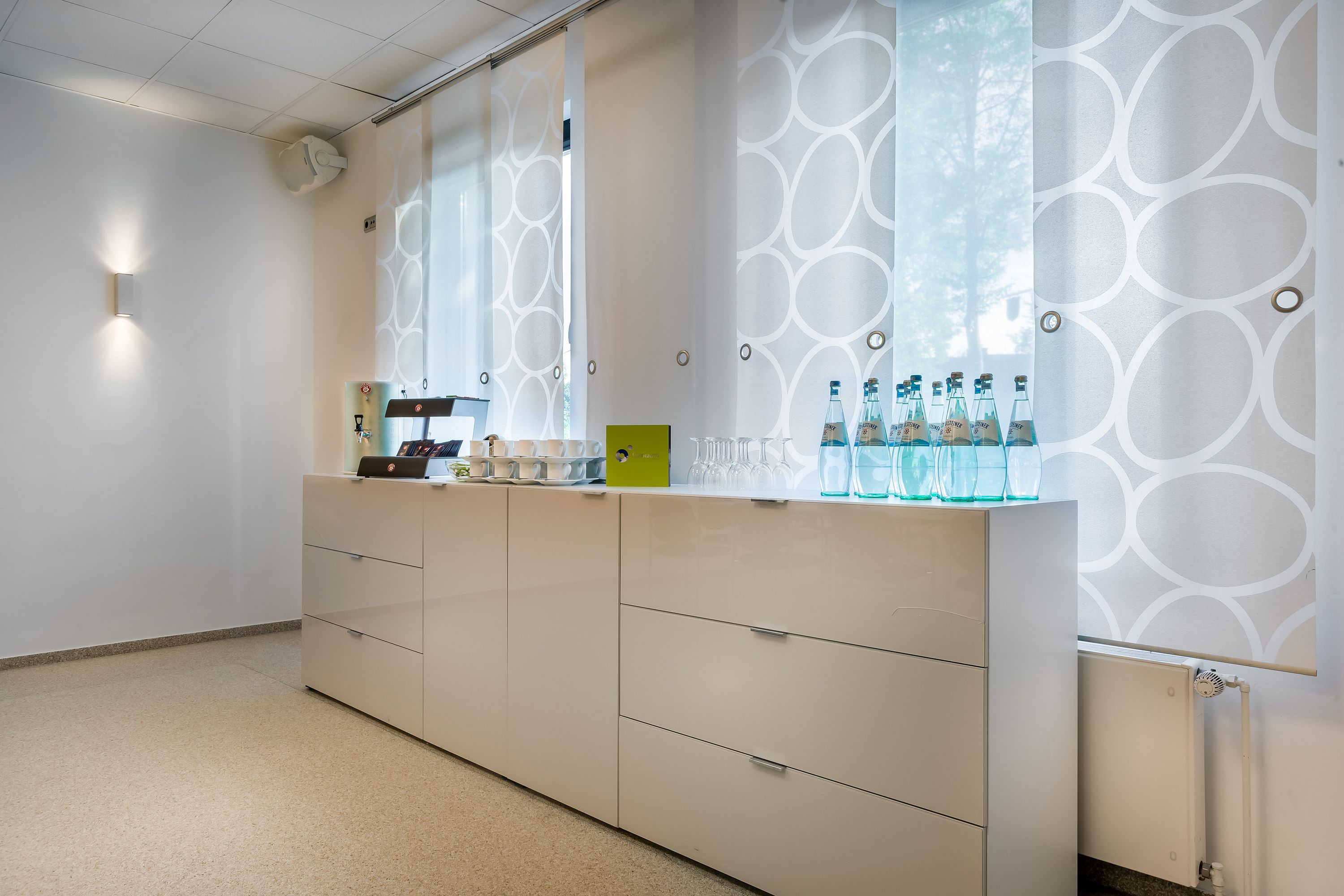 Zona de recepción de un hotel moderno con diseño minimalista, destacando un mostrador con botellas de vidrio y un letrero verde, además de una pared con un diseño original.