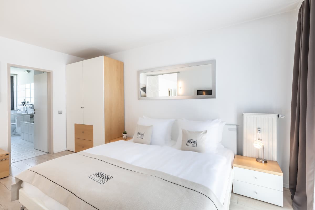 Une chambre d’hôtel moderne avec un grand lit, une table de chevet avec une lampe, une armoire et un miroir au mur.