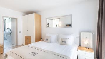 Quarto de hotel moderno com uma cama grande, uma mesa de cabeceira com abajur, um guarda-roupa e um espelho na parede.