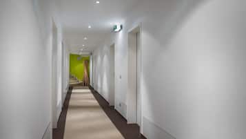 Ein moderner Hotelgang mit weißen Wänden, einem beigen Teppich und einer grünen Akzentwand am Ende.