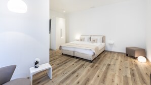 Un dormitorio moderno con cama, mesitas de noche y un pequeño rincón de descanso.