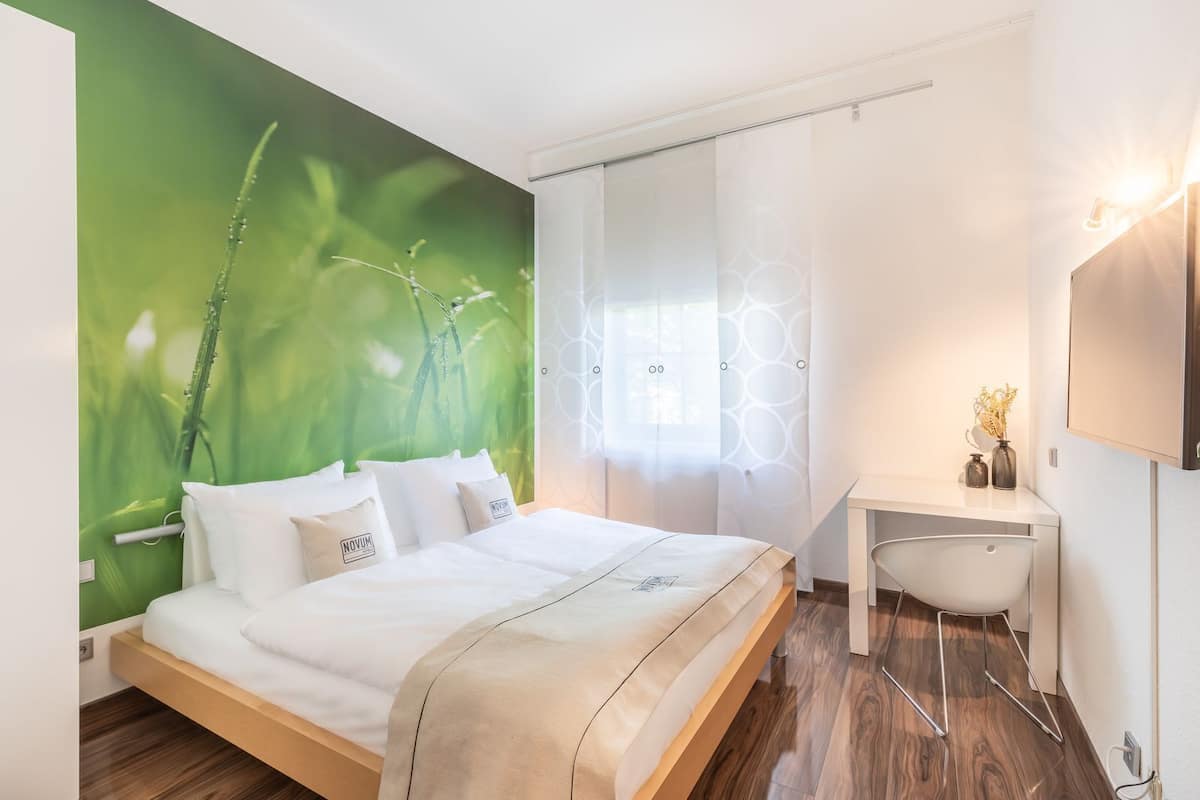 Une chambre moderne avec un lit, un bureau et un mur décoré d’une fresque verte.