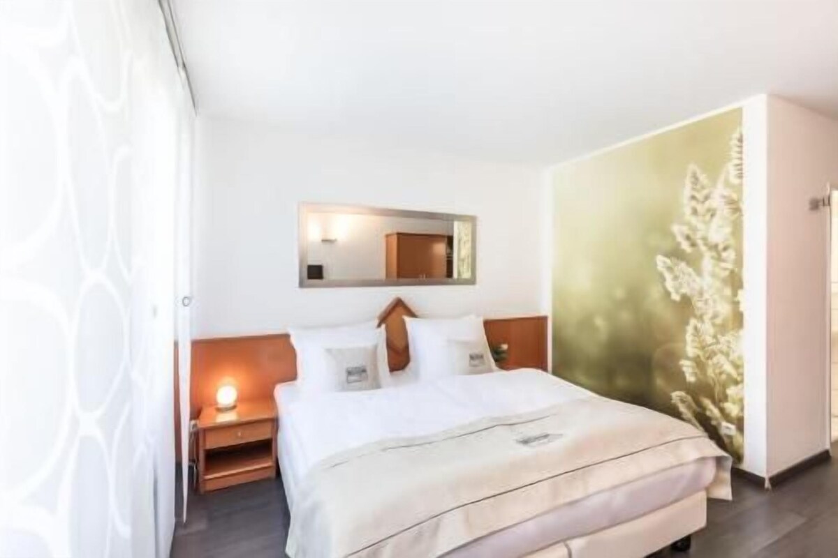 A hotel room with a bed, bedside table, nightstand, and a wall-mounted mirror.