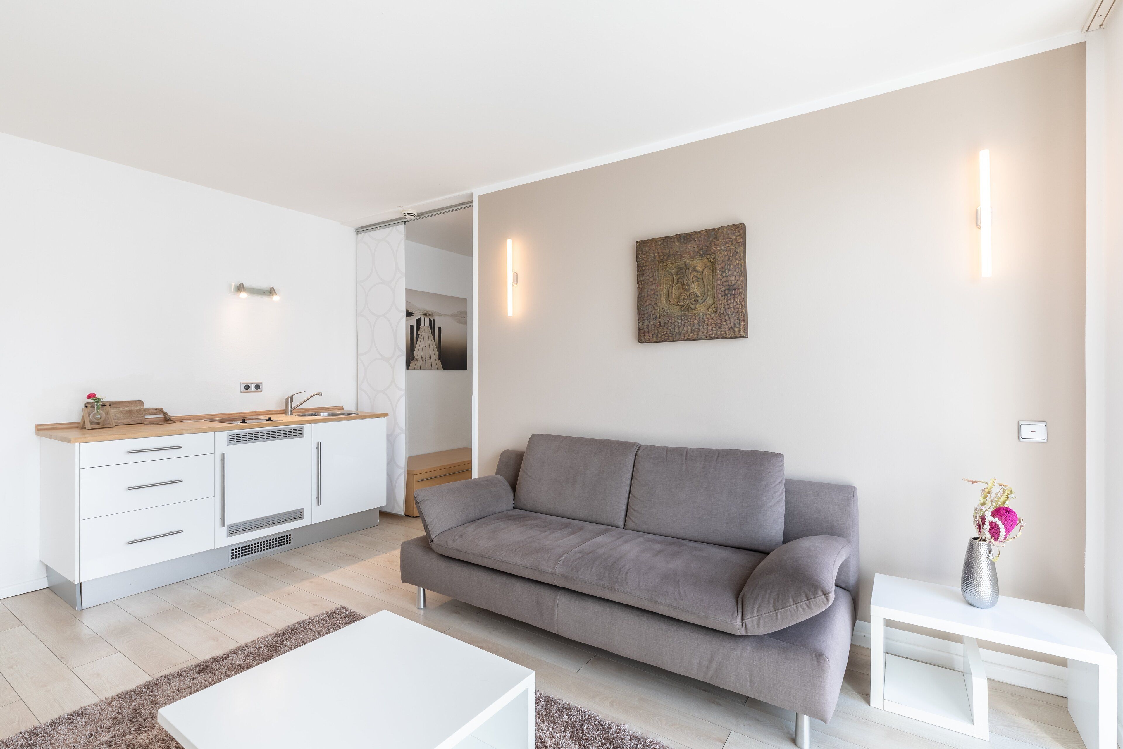Una sala de estar moderna con un sofá gris, una mesa de centro blanca y una mesita auxiliar blanca con un jarrón.
