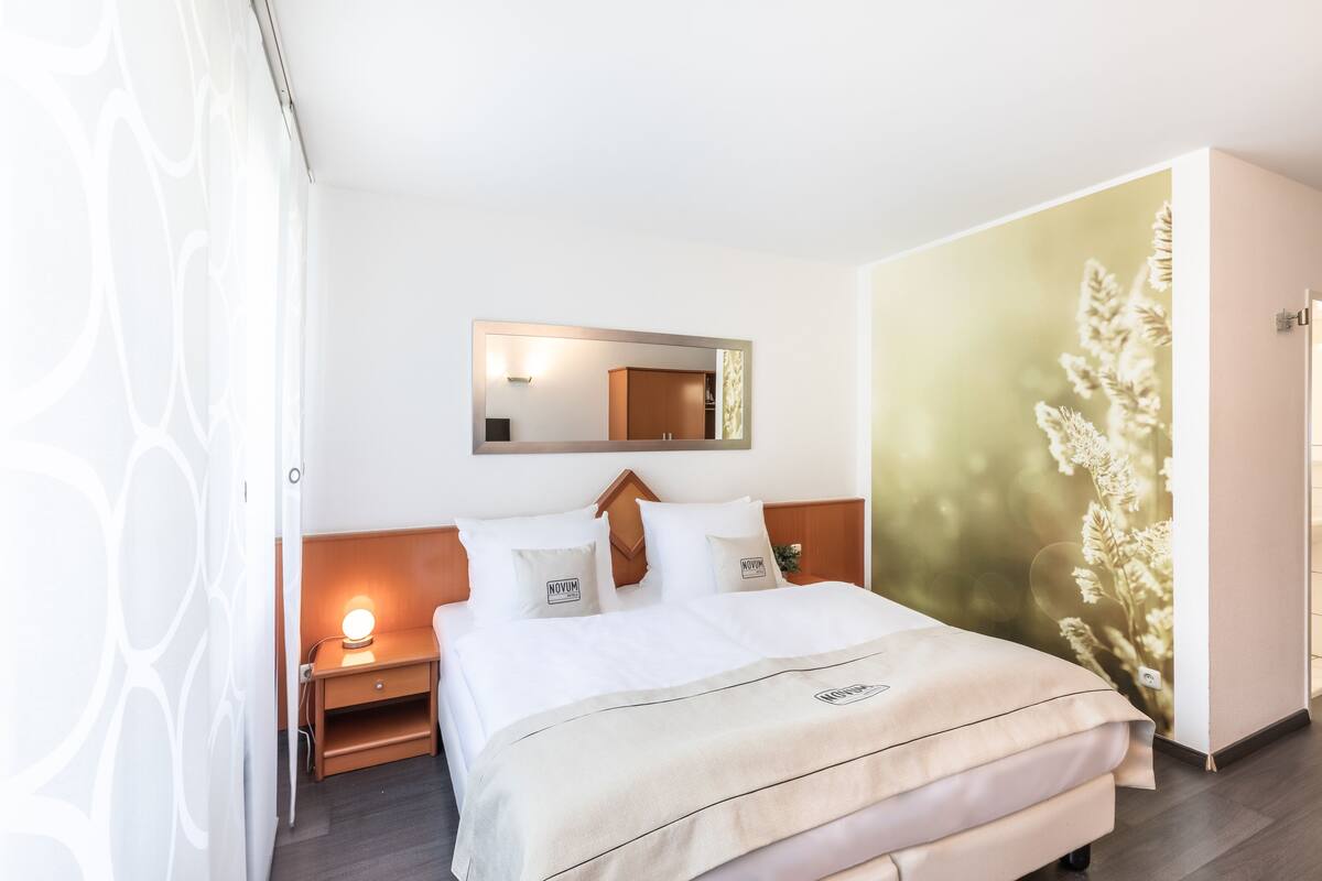 Une chambre d’hôtel bien rangée, avec un lit, une table de chevet et un miroir au-dessus.