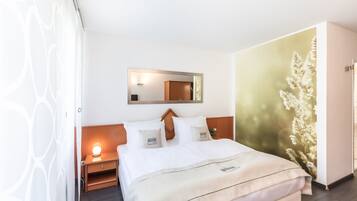Una habitación de hotel con cama, mesita de noche y espejo adosado a la pared.