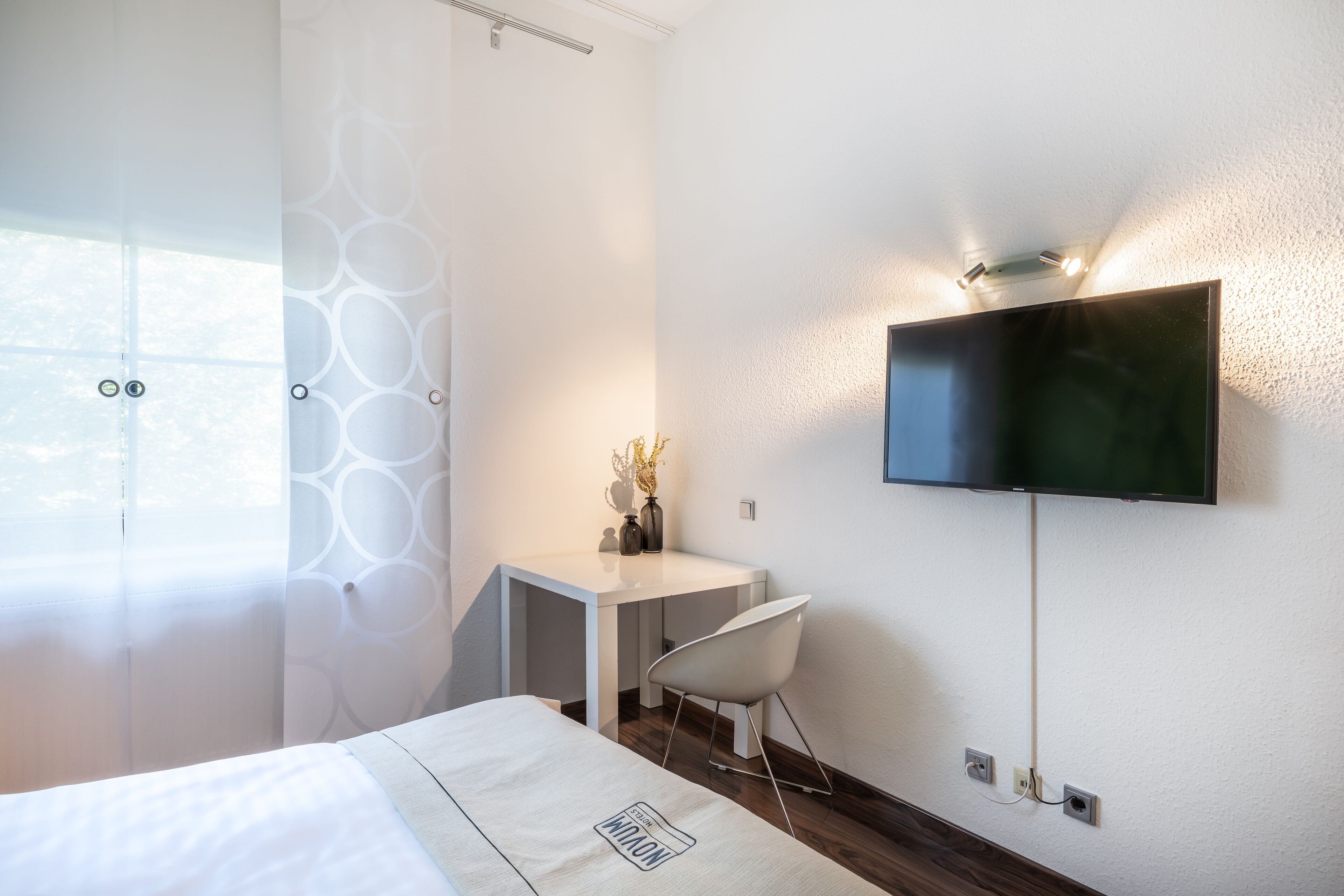 Een moderne hotelkamer met een bed, een bureau, een stoel en een aan de muur bevestigde televisie.
