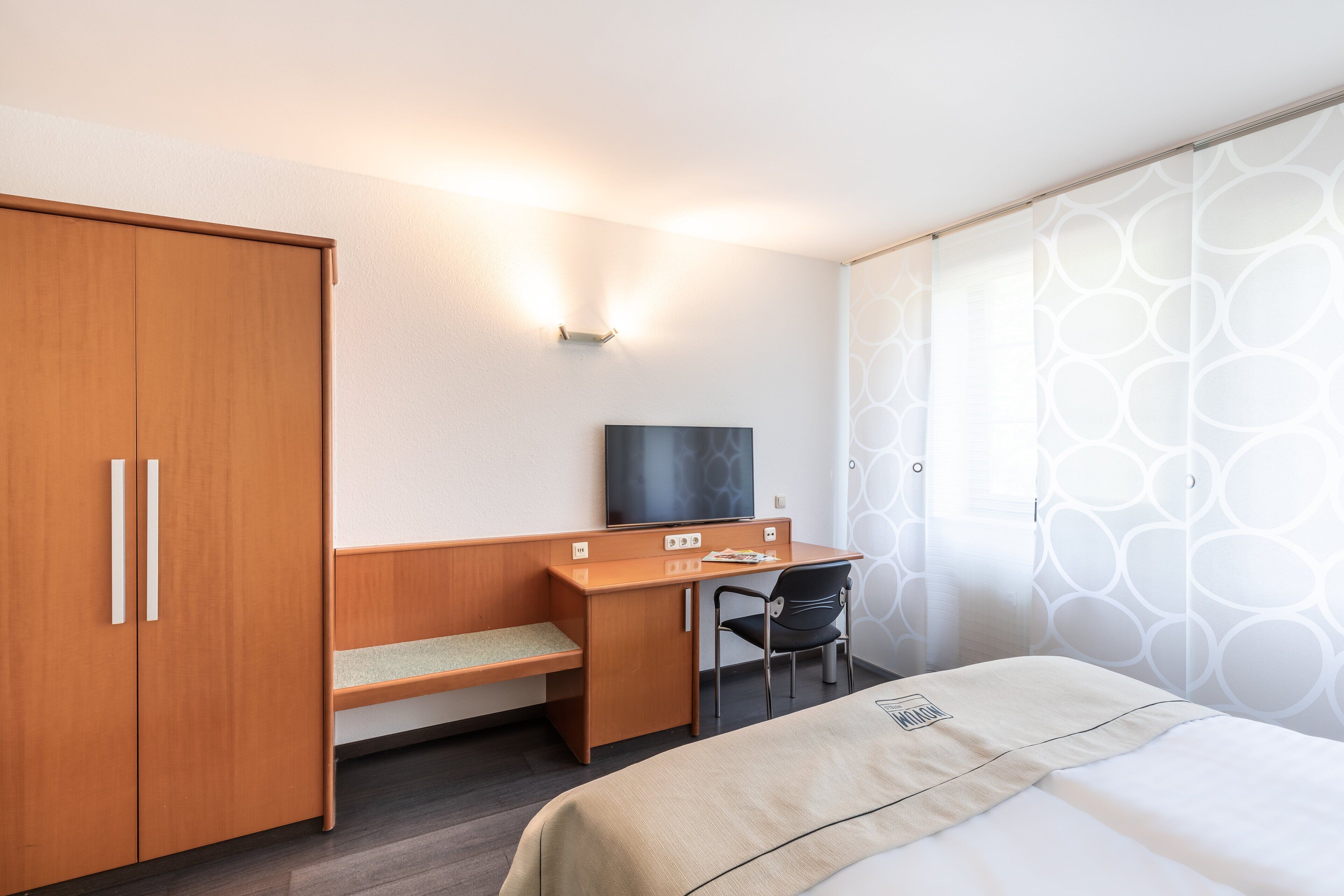 Una habitación de hotel con cama, escritorio con silla, armario y televisor.