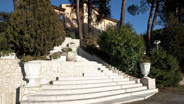 A stone staircase leading up to a building with a stone wall and a large white urn at the top. - Villa Hotel del Sole (Chiusi)