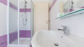 A bathroom with a shower, a sink, and a glass shelf with toiletries.