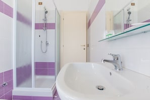 A bathroom with a shower, a sink, and a glass shelf with toiletries. - Villa Hotel del Sole (Chiusi)