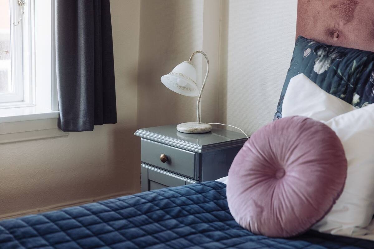 A bedroom with a bed, a nightstand, a lamp, and a window with curtains.