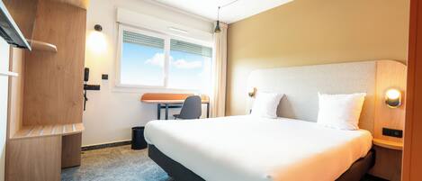 A hotel room with a large bed, a desk, and a chair.