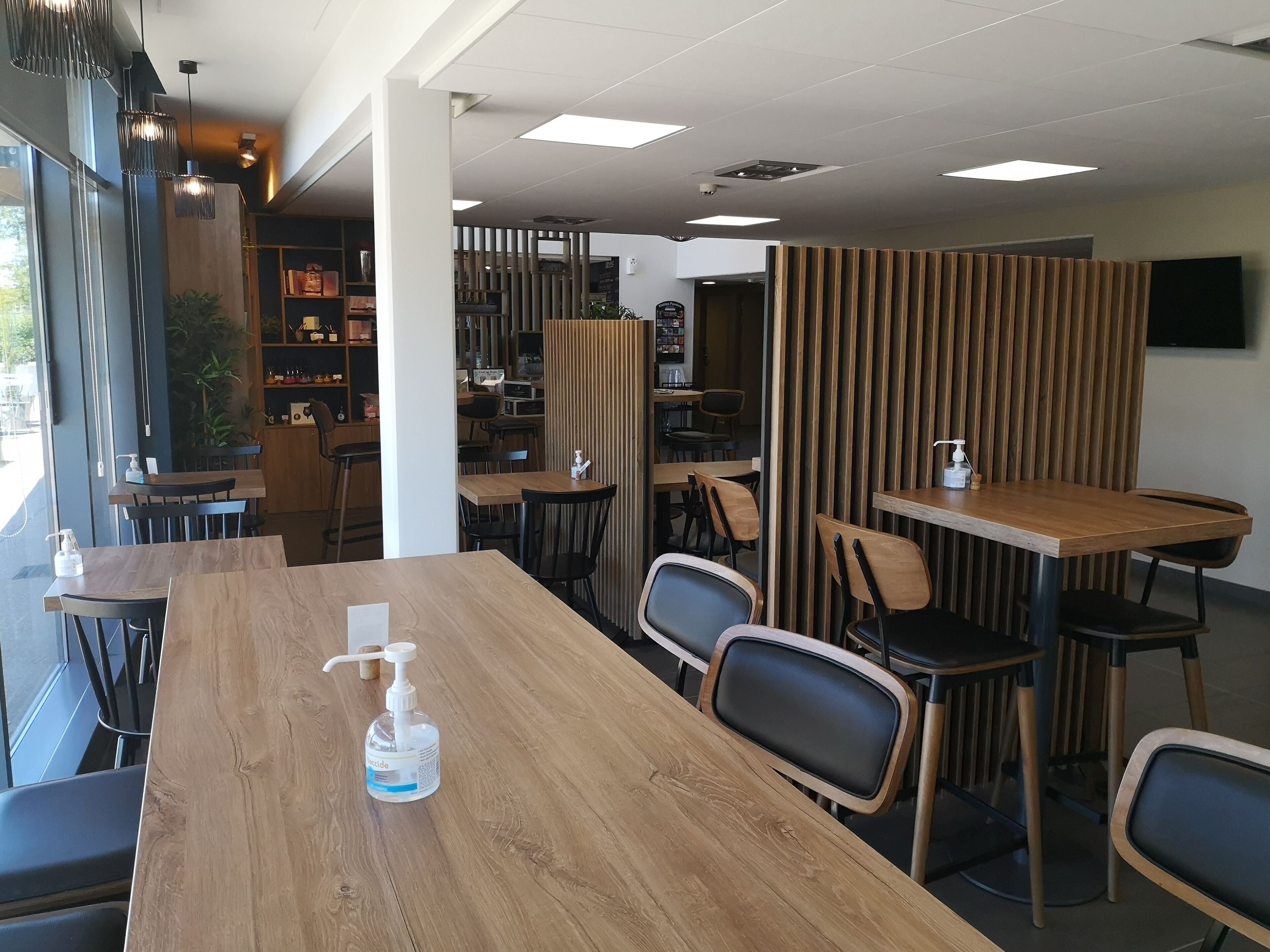 Een modern restaurantinterieur met houten tafels en stoelen, een scheidingswand en een hangende televisie.