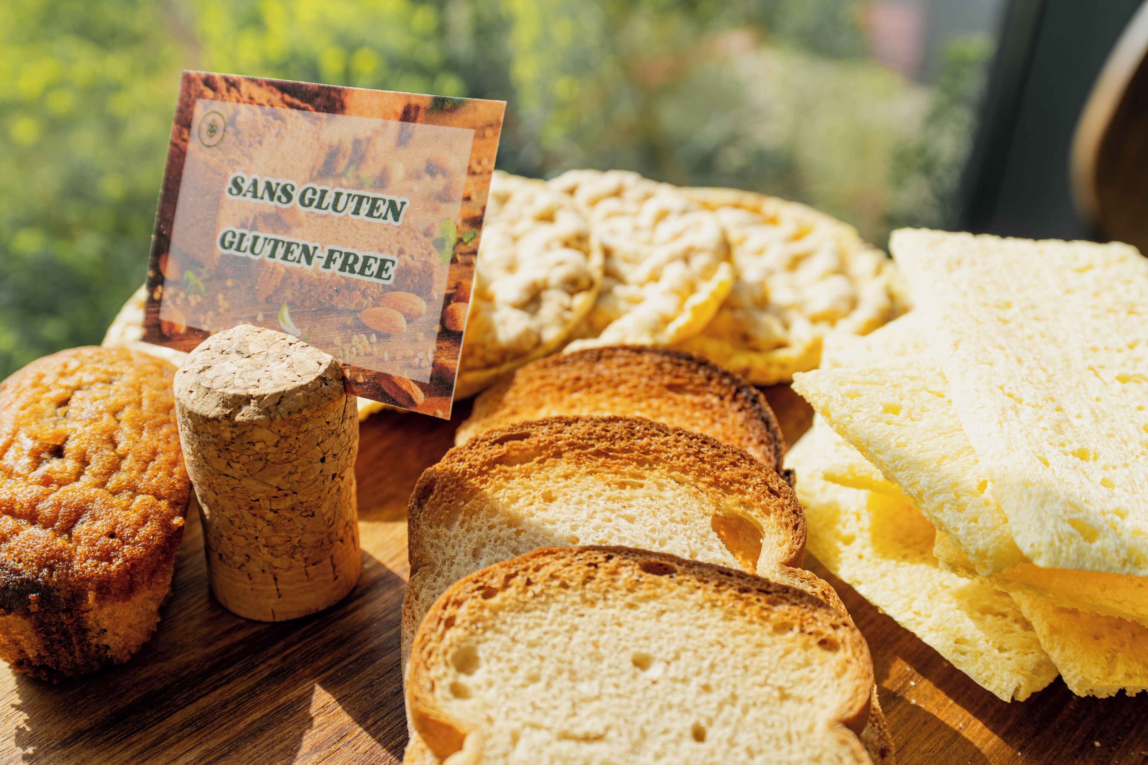 A variety of gluten-free breads and muffins on a wooden board with a sign indicating they are gluten-free.