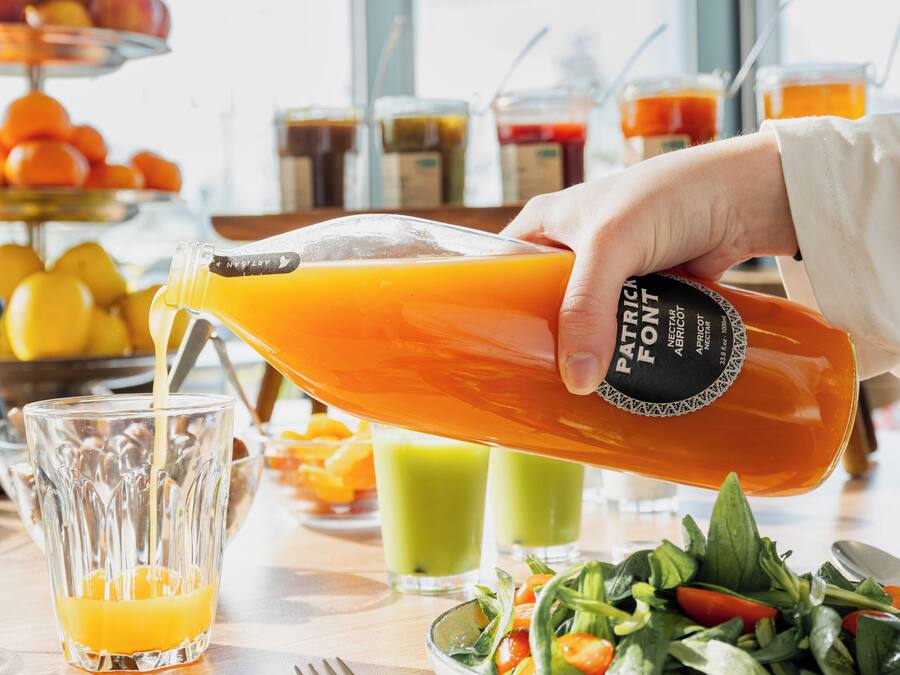 A hand pouring orange juice into a glass.