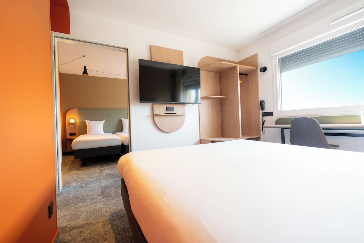 Una habitación de hotel moderna con una cama grande, un televisor de pantalla plana montado en la pared, un escritorio con una silla y una ventana con vistas al cielo.