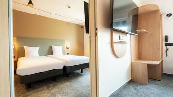 A hotel room with two beds, a wooden bench, a mirror, and a wall-mounted phone.