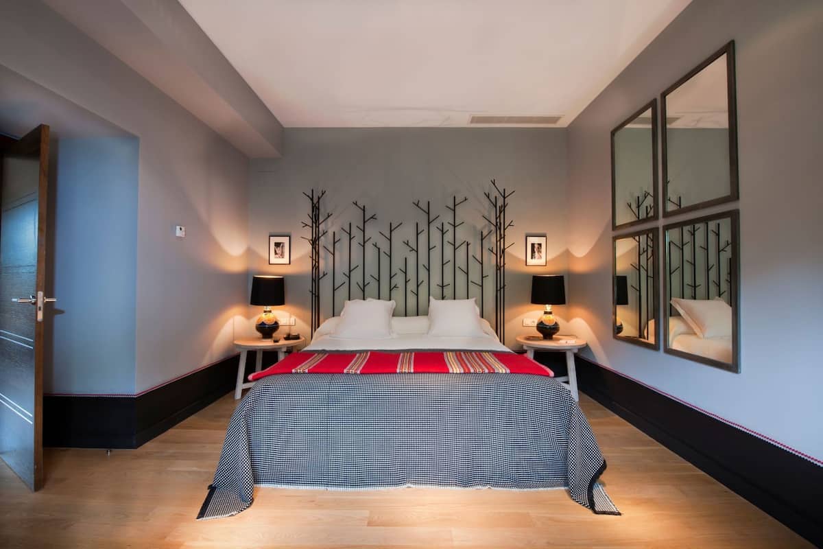 Une chambre à coucher moderne avec un lit, des tables de chevet, une couvre-lit aux motifs rouges et noirs, et des éléments de décoration fixés au mur.