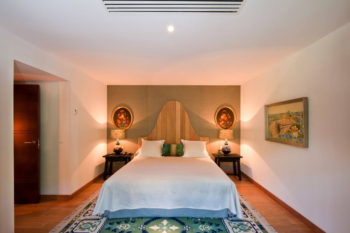 Une chambre d’hôtel avec un lit, deux tables de chevet, une tête de lit, un tableau et un tapis à motifs.