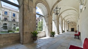 Un pasillo con arcos de piedra, plantas en macetas y asientos rojos.