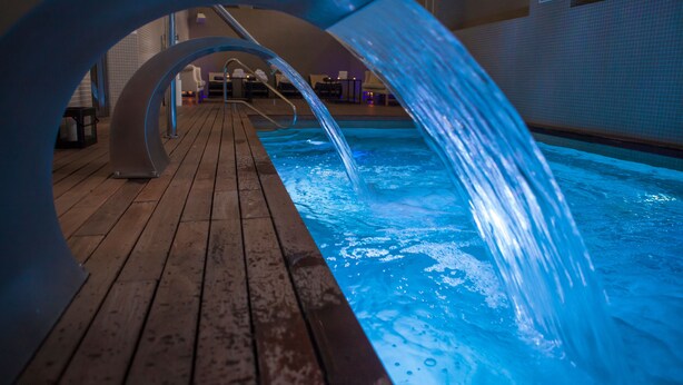 Zona de piscina con terraza de madera y fuente.