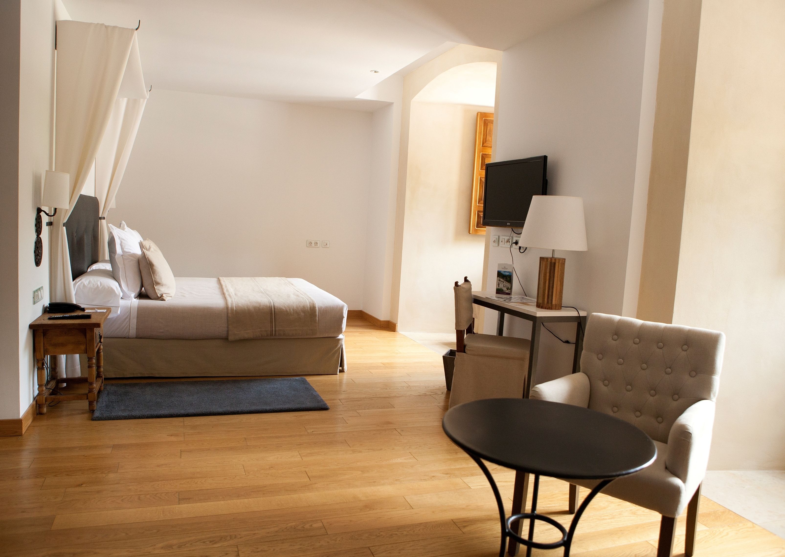 A hotel room with a bed, bedside table, lamp, chair, and a TV on the wall.