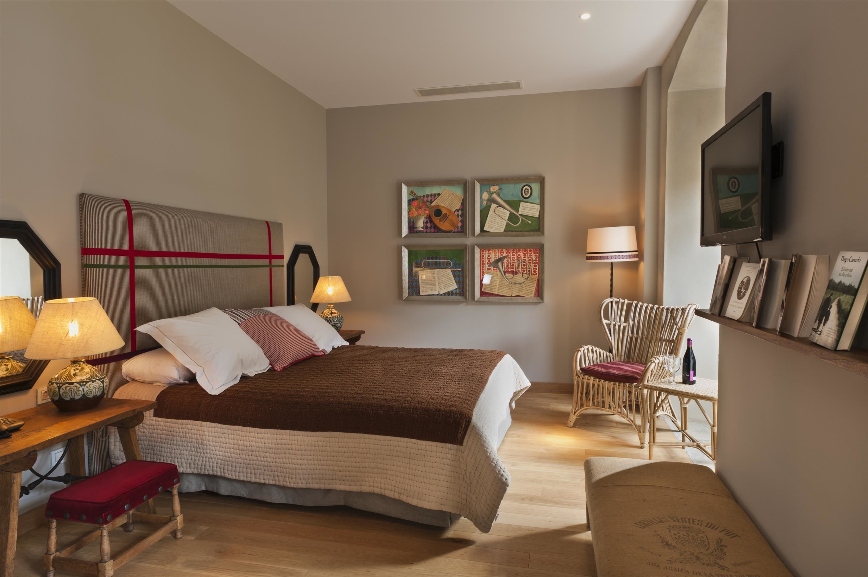 A bedroom with a bed, bedside lamps, a chair, a table, and wall art.
