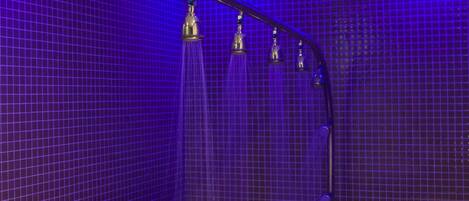 Une salle de spa équipée d’une table de massage, d’une douche et d’un mur recouvert de carreaux.