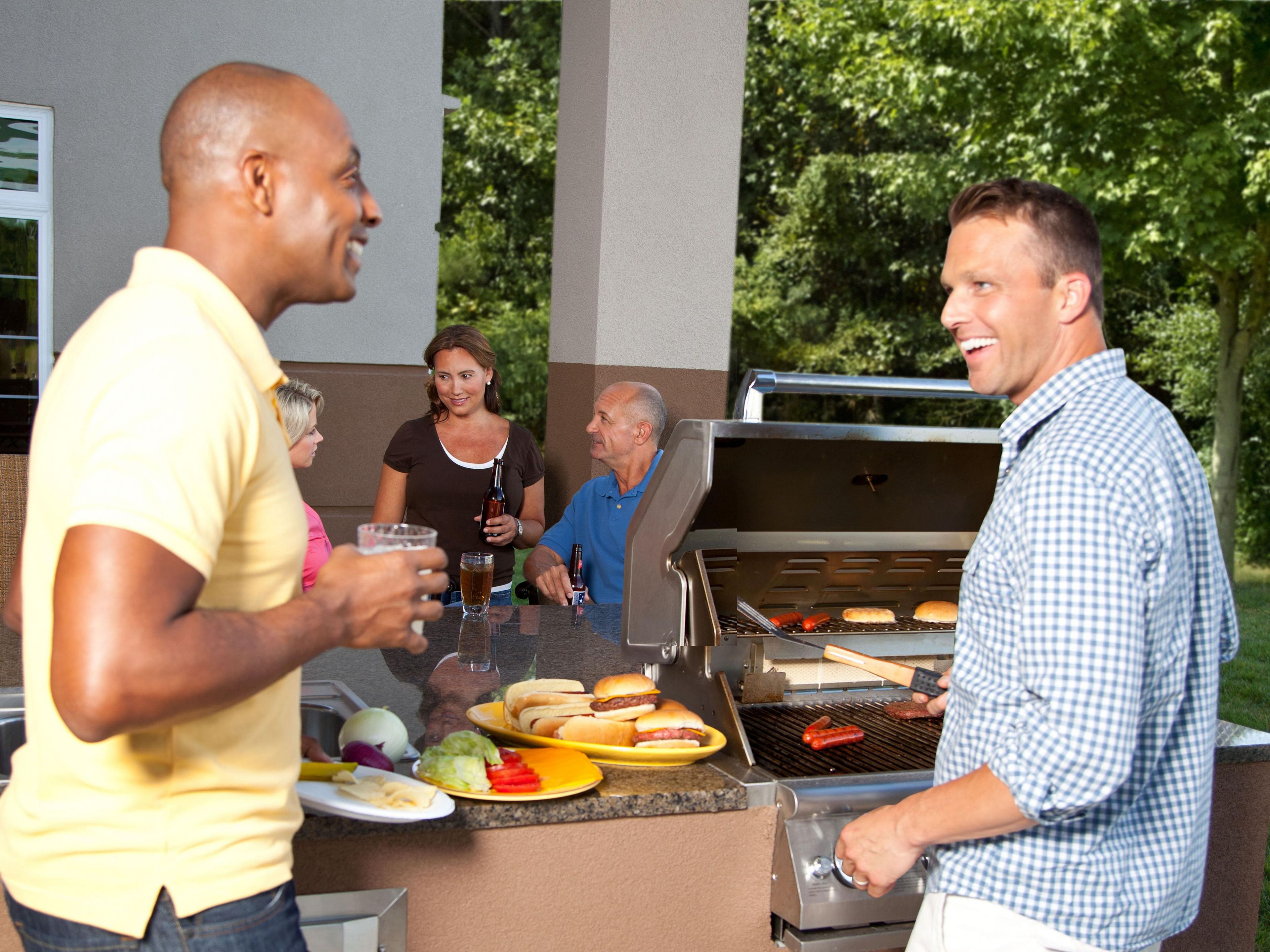 A group of people at an outdoor barbecue with a grill and food on the counter.