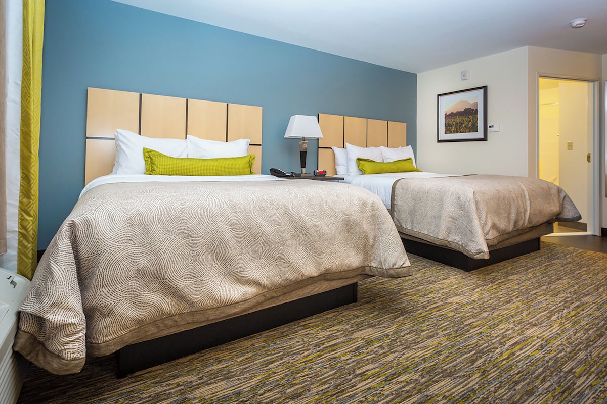 A hotel room with two beds, a headboard, a lamp, a framed picture on the wall, and a carpeted floor.