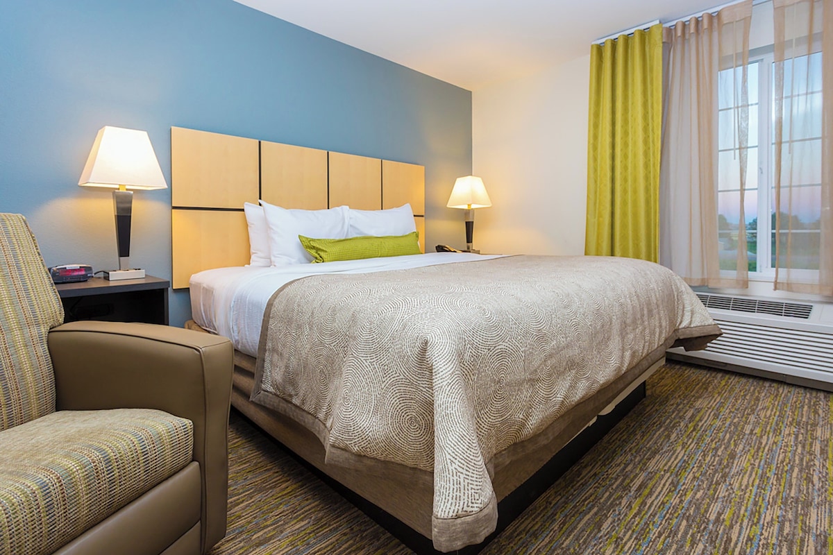 A hotel room with a bed, two bedside lamps, a chair, and a window with curtains.