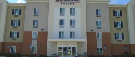 Un hotel de varios pisos con entrada central, múltiples ventanas en cada planta y un cartel que dice 'CANDLEWOOD SUITES'.