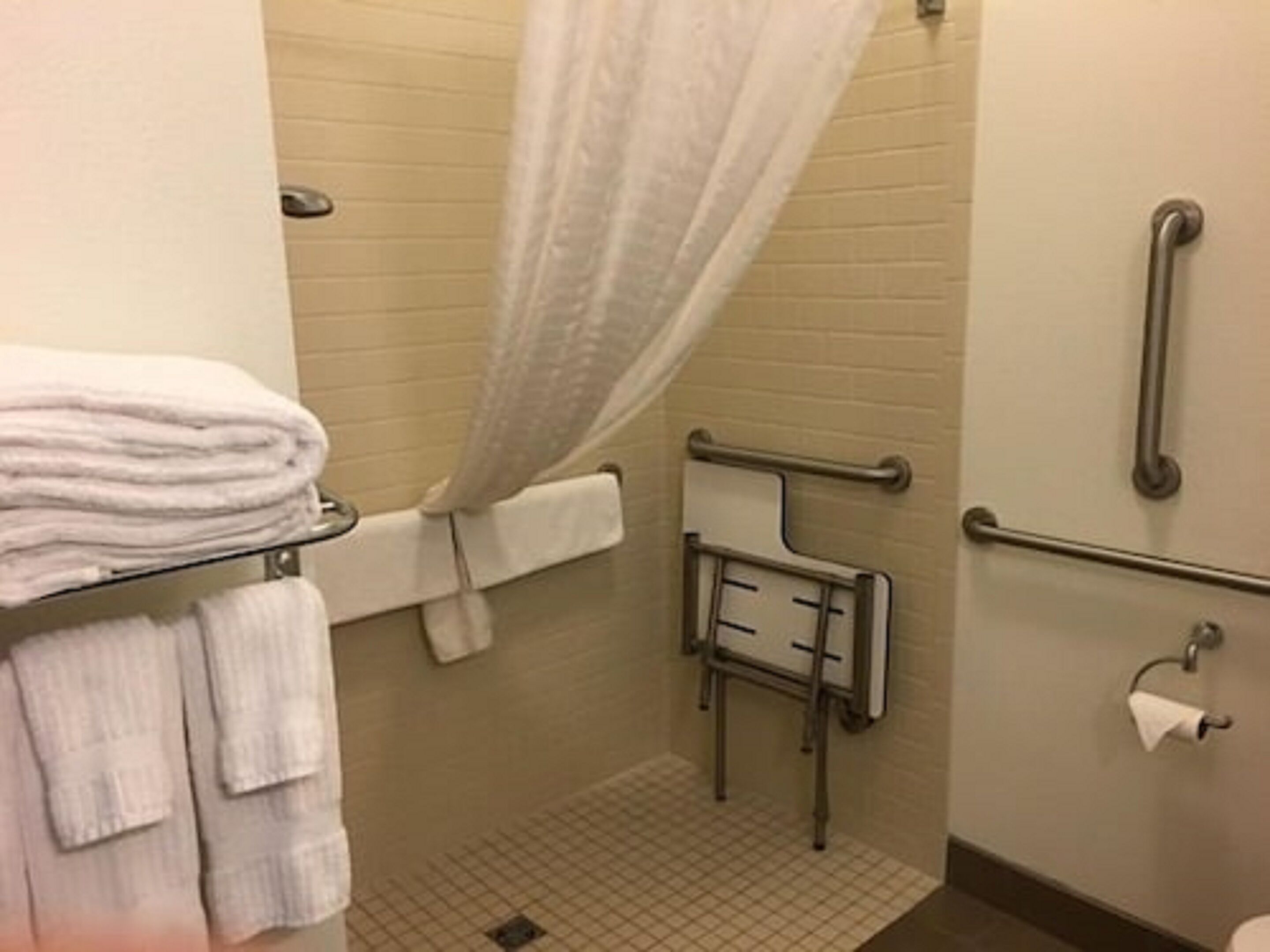 A bathroom with a shower, a towel rack, a grab bar, and a toilet paper holder.