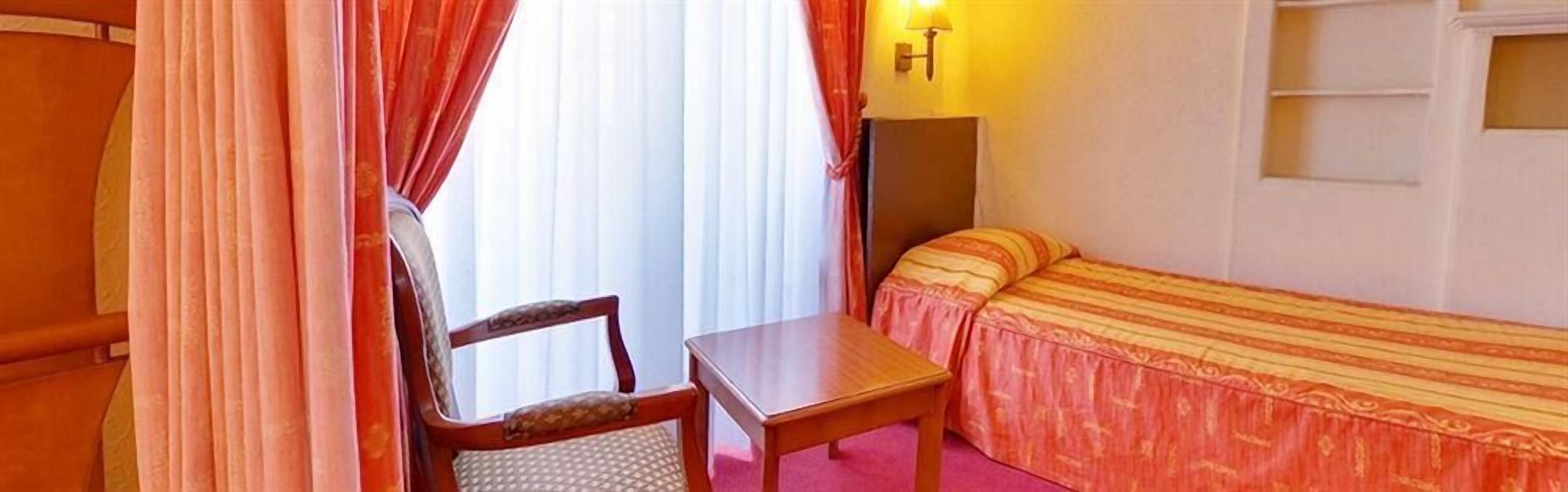 A room with a bed, a chair, a table, and a lamp.