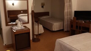 Una camera d'albergo con un letto, una scrivania con una sedia, una televisione, un tavolino con un vaso e uno specchio.