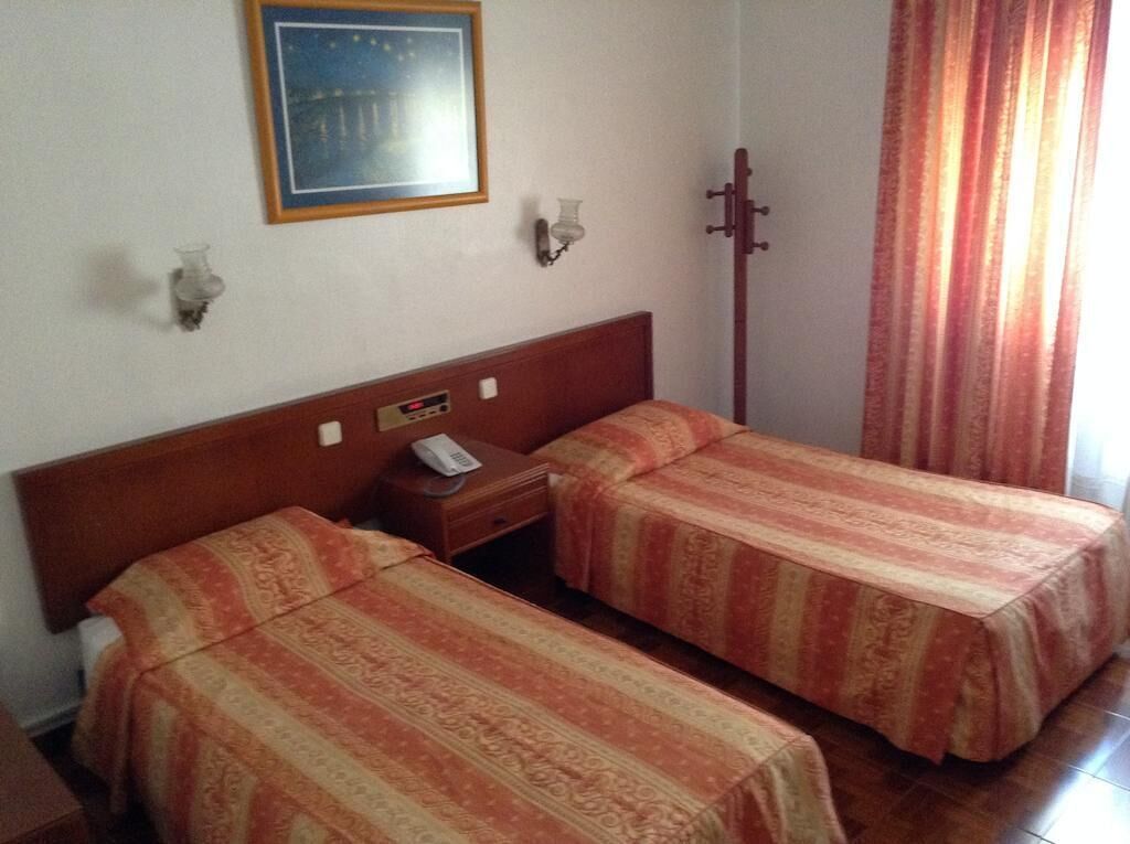A hotel room with two single beds, a nightstand, a telephone, a framed picture on the wall, and a curtain.