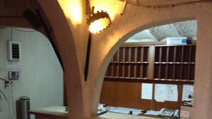 Una stanza con soffitto a volta, una finestra con vetri a inferriata e una scrivania in legno con documenti.