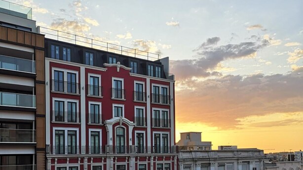 Un edificio a più piani con facciata rossa e decorazioni bianche, caratterizzato da balconi e ampie finestre.