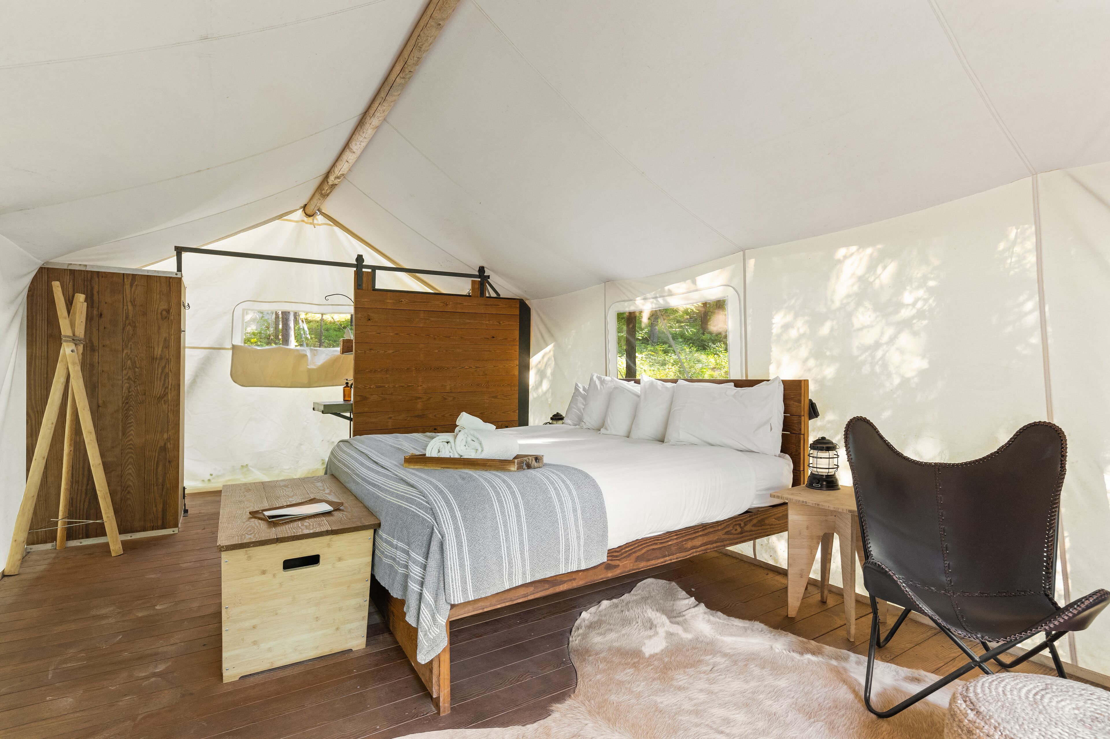 A tented room with a bed, a wooden chest, a chair, and a small table with a lantern.