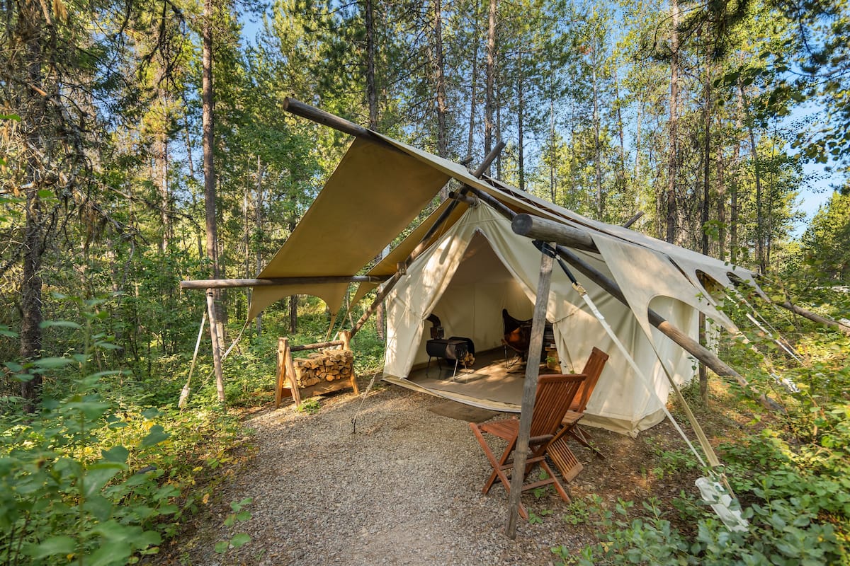 Tienda de campaña montada en un bosque, con un hogar y sillas en su interior.