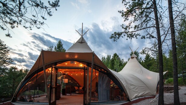 A large, modern tent with a glass entrance, surrounded by trees and gravel. - Under Canvas Glacier (Coram)