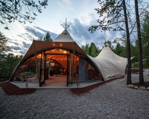 A large, modern tent with a glass entrance, surrounded by trees and gravel.