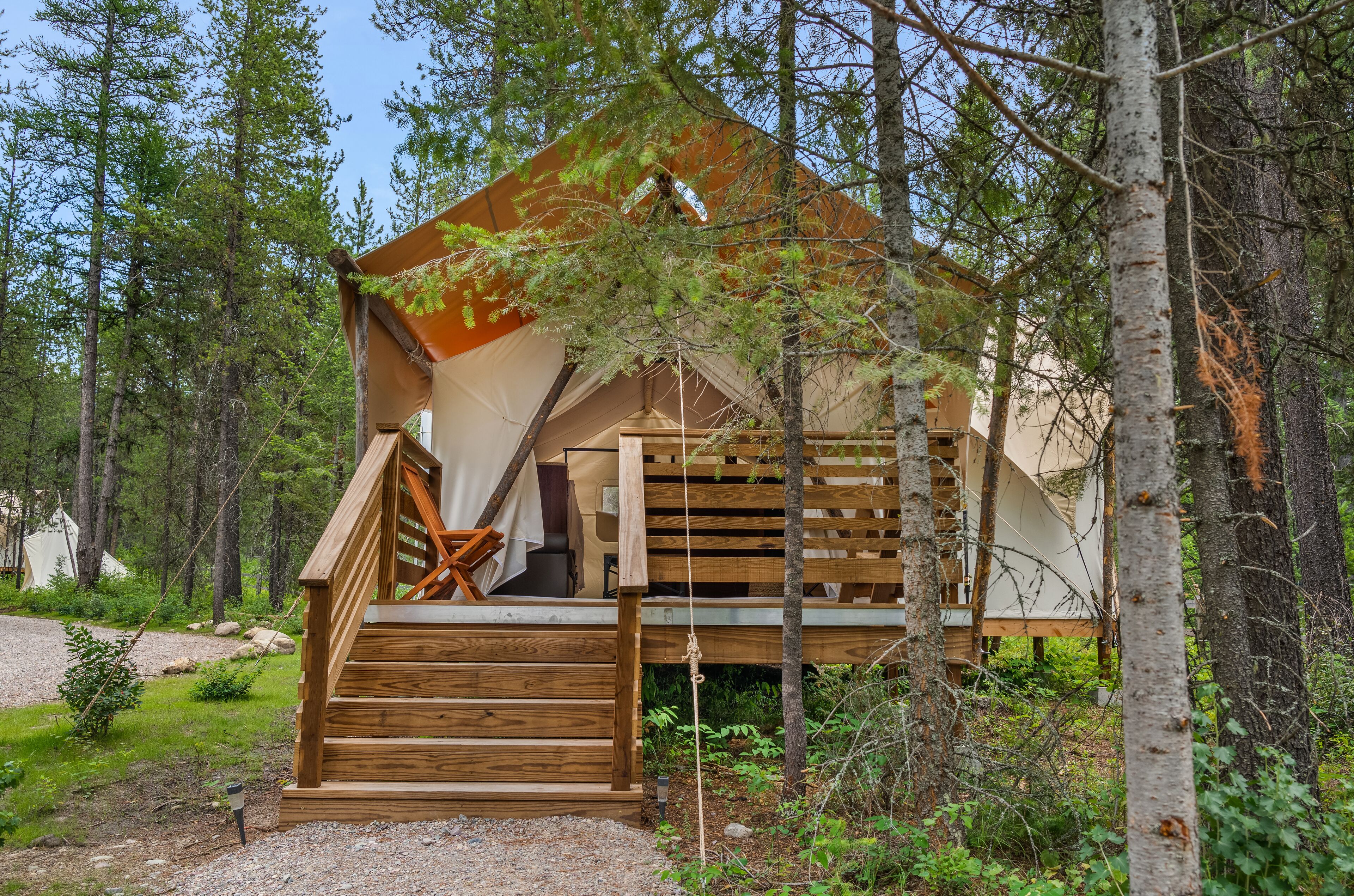 Une cabane avec un escalier en bois menant à une terrasse, le tout entouré d’arbres.